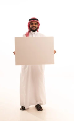 إعلانات وعروض تسويقية، استخدام لوحات توضيحية ووسائل تعليمية، بورتريه لرجل عربي خليجي سعودي يرتدي الشماغ والثوب التقليدي يحمل بيده لوح ابيض كبير (موك اب فارغ)، النظر الى الكاميرا بايماءات السعادة والسرور، الطول الكامل للجسم، خلفية بيضاء