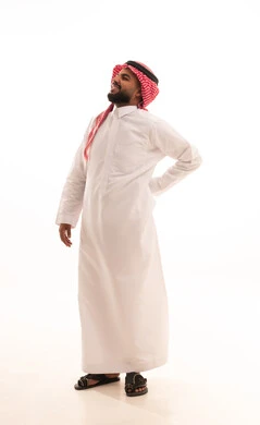 Spinal and back pain, a portrait of a Saudi Arabian Gulf man wearing a ghutrah and traditional thobe, placing his hand on his back with expressions of bending, gestures of pain and discomfort, fatigue and exhaustion, and a sense of illness, the need for treatment and a doctor's visit, full-body image, white background.