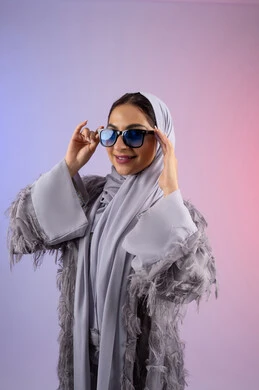 The concept of femininity, elegance and beauty, enjoying owning modern accessories, an Emirati woman wearing an abaya and glasses looking at the camera with an expression of pleasure, a portrait of a veiled Saudi Arabian Gulf woman trying on new sunglasses, a colorful background