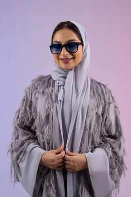 The concept of femininity, elegance and beauty, enjoying owning modern accessories, an Emirati woman wearing an abaya and glasses looking at the camera with an expression of pleasure, a portrait of a veiled Saudi Arabian Gulf woman trying on new sunglasses, a colorful background