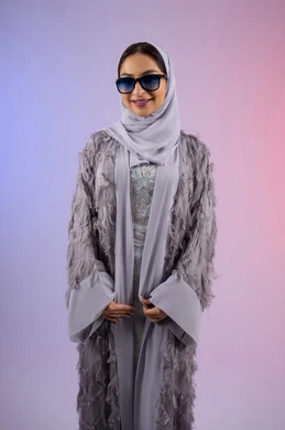 اقتناء اكسسوارات عصرية, مفهوم الانوثة والأناقة والجمال, سيدة اماراتية ترتدي عباءة ونظارة تنظر إلى الكاميرا بتعابير السرور, بورتريه لامرأة عربية خليجية سعودية محجبة تقوم بتجربة النظارات الشمسية الجديدة, خلفية ملونة