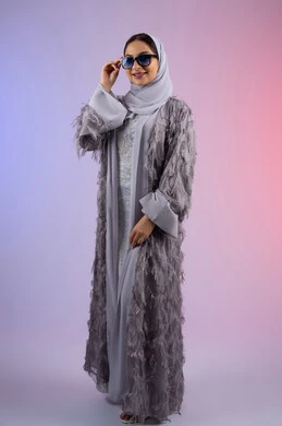 عرض الأزياء والاكسسوات النسائية العصرية، الاهتمام بالمظهر الخارجي، مفهوم الأناقة والجمال, سيدة اماراتية ترتدي عباءة تنظر إلى الكاميرا بتعابير الأنوثة والسرور, بورتريه لامرأة عربية خليجية سعودية محجبة تضع نظارات شمسية, الجسم بالطول الكامل، خلفية ملونة