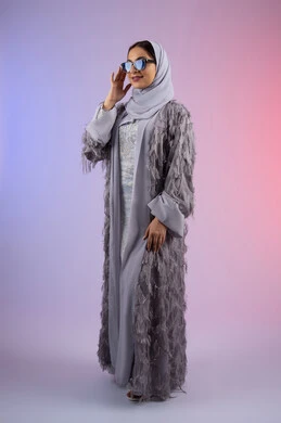 الوقوف بتعابير الأنوثة والسرور, التسويق للأزياء والاكسسوارات النسائية العصرية، مفهوم الأناقة والجمال, الاهتمام بالمظهر الخارجي، سيدة اماراتية مبتسمة ترتدي عباءة، بورتريه لامرأة عربية خليجية سعودية محجبة تضع نظارات شمسية, الجسم بالطول الكامل، خلفية ملونة