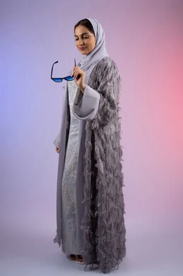 الاستمتاع بامتلاك اكسسوارات عصرية، الوقوف بتعابير الأنوثة والسرور, مفهوم الأناقة والجمال, الاهتمام بالمظهر الخارجي، سيدة اماراتية مبتسمة ترتدي عباءة، بورتريه لامرأة عربية خليجية سعودية محجبة تضع نظارات شمسية, الجسم بالطول الكامل، خلفية ملونة