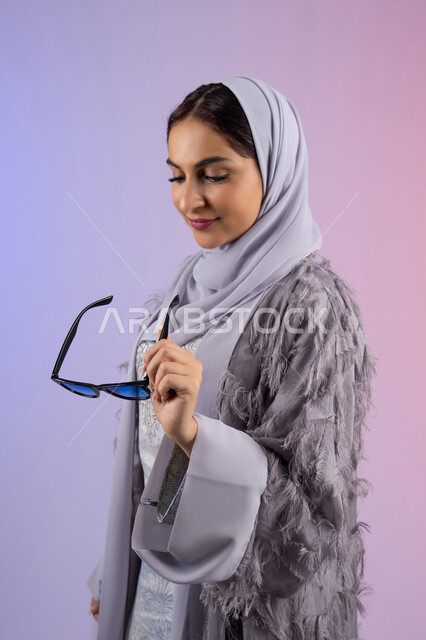 عرض الأزياء والموديلات الحديثة، شراء اكسسوارات نسائية عصرية, مفهوم الانوثة والأناقة والجمال, سيدة اماراتية ترتدي عباءة ونظارة ملونة, بورتريه لامرأة عربية خليجية سعودية محجبة تحمل بيدها نظارات شمسية, خلفية ملونة