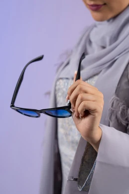 التسويق للمنتجات المحلية، عرض الأزياء والموديلات الحديثة، شراء اكسسوارات نسائية عصرية, مفهوم الانوثة والأناقة والجمال, سيدة اماراتية ترتدي عباءة رمادية, بورتريه مقرب لامرأة عربية خليجية سعودية محجبة تحمل بيدها نظارات شمسية, خلفية ملونة
