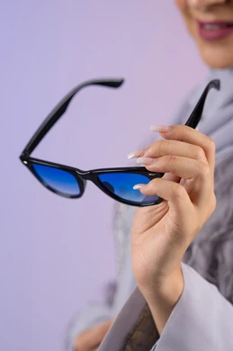 شراء اكسسوارات نسائية عصرية, التسويق للمنتجات المحلية، عرض الأزياء والموديلات الحديثة، مفهوم الانوثة والأناقة والجمال, سيدة اماراتية ترتدي عباءة رمادية, بورتريه مقرب لامرأة عربية خليجية سعودية محجبة تمسك بيدها نظارات شمسية زرقاء, خلفية ملونة