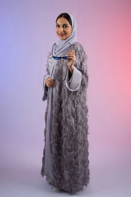 الاهتمام بالمظهر الخارجي، عرض الأزياء والاكسسوات النسائية العصرية، مفهوم الأناقة والجمال, سيدة اماراتية ترتدي عباءة تنظر إلى الكاميرا بتعابير الأنوثة والسرور, بورتريه لامرأة عربية خليجية سعودية محجبة تضع نظارات شمسية, الجسم بالطول الكامل، خلفية ملونة