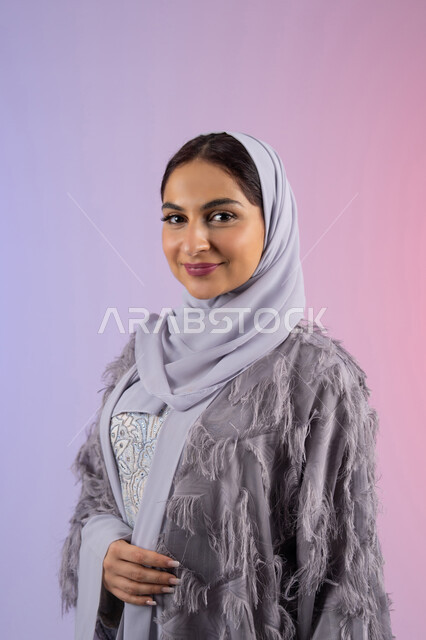 الاهتمام بالمظهر الخارجي، مفهوم الانوثة والأناقة والجمال, عرض أزياء نسائية عصرية، سيدة اماراتية مبتسمة ترتدي عباءة، بورتريه لامرأة عربية خليجية سعودية محجبة تنظر إلى الكاميرا بتعابير السرور والسعادة, خلفية ملونة