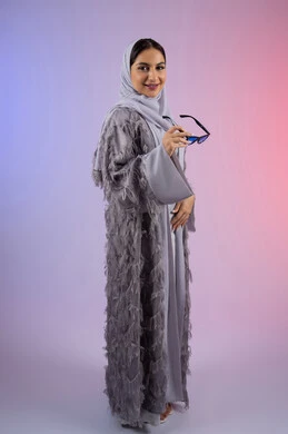 النظر إلى الكاميرا بتعابير الأنوثة والسرور, الاستمتاع بامتلاك اكسسوارات عصرية، مفهوم الأناقة والجمال, الاهتمام بالمظهر الخارجي، سيدة اماراتية مبتسمة ترتدي عباءة، بورتريه لامرأة عربية خليجية سعودية محجبة تضع نظارات شمسية, الجسم بالطول الكامل، خلفية ملونة