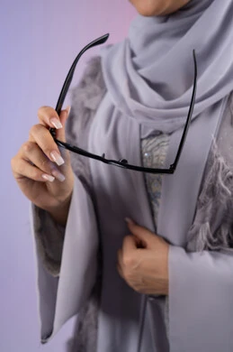 التسويق للمنتجات المحلية، عرض الأزياء والموديلات الحديثة، شراء اكسسوارات نسائية عصرية, مفهوم الانوثة والأناقة والجمال, سيدة اماراتية ترتدي عباءة رمادية, بورتريه مقرب لامرأة عربية خليجية سعودية محجبة تحمل بيدها نظارات شمسية, خلفية ملونة