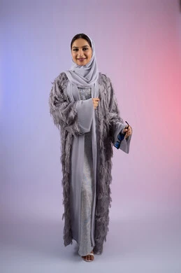 النظر إلى الكاميرا بتعابير الأنوثة والسرور, الاستمتاع بامتلاك اكسسوارات عصرية، مفهوم الأناقة والجمال, الاهتمام بالمظهر الخارجي، سيدة اماراتية مبتسمة ترتدي عباءة، بورتريه لامرأة عربية خليجية سعودية محجبة تضع نظارات شمسية, الجسم بالطول الكامل، خلفية ملونة