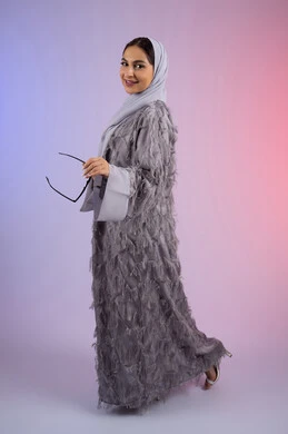 الاستمتاع بامتلاك اكسسوارات عصرية، الوقوف بتعابير الأنوثة والسرور, مفهوم الأناقة والجمال, الاهتمام بالمظهر الخارجي، سيدة اماراتية مبتسمة ترتدي عباءة، بورتريه لامرأة عربية خليجية سعودية محجبة تضع نظارات شمسية, الجسم بالطول الكامل، خلفية ملونة