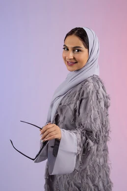 شراء اكسسوارات عصرية, مفهوم الانوثة والأناقة والجمال, سيدة اماراتية ترتدي عباءة ونظارة تنظر إلى الكاميرا بتعابير السرور, بورتريه لامرأة عربية خليجية سعودية محجبة تحمل بيدها النظارات الشمسية الجديدة, خلفية ملونة