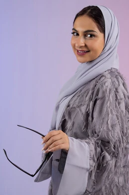 اقتناء اكسسوارات عصرية, مفهوم الانوثة والأناقة والجمال, سيدة اماراتية ترتدي عباءة ونظارة تنظر إلى الكاميرا بتعابير السرور, بورتريه لامرأة عربية خليجية سعودية محجبة تقوم بتجربة النظارات الشمسية الجديدة, خلفية ملونة