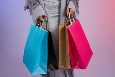 السعادة والمتعة بالتسوق وشراء المستلزمات الجديدة، الترويج للمنتجات والماركات العالمية، شابة سعودية ترتدي عباءة، بورتريه مقرب لامرأة عربية خليجية اماراتية تحمل بيدها أكياس تسوق ملونة، خلفية ملونة