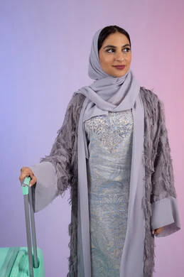 Summer vacation tourism, preparing for a fun summer trip, portrait of a smiling Saudi Arabian Gulf young woman wearing an abaya and holding a suitcase, Emirati woman looking at something with confident gestures, feeling happy and joyful, colorful background.