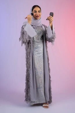 الاستمتاع بوضع الميك اب، الاهتمام بالجمال والمظهر الخارجي, التسويق لمساحيق التجميل, مفهوم التزين والتجمل, بورتريه لامرأة عربية خليجية إماراتية محجبة ترتدي العباءة تقوم باستخدام فرشاة أحمر الخدود, شابة سعودية تضع مكياج تتوريال, الجسم بالطول الكامل، خلفية ملونة