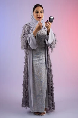 احتراف واتقان وضع الميك اب، الاهتمام بالجمال والمظهر الخارجي, التسويق لمساحيق التجميل, مفهوم التزين والتجمل, بورتريه لامرأة عربية خليجية إماراتية محجبة ترتدي العباءة تقوم باستخدام قلم أحمر الشفاه, شابة سعودية تضع مكياج تتوريال, الجسم بالطول الكامل، خلفية ملونة