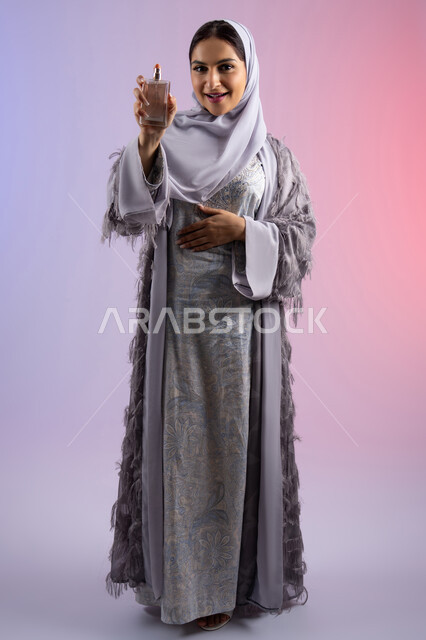 عطور عربية خليجية، الترويج للعطور والزيوت الطبيعية المحلية، مفهوم التعطر والتطيب، استخدام العود العطري، سيدة اماراتية تسوق للمنتجات العطرية، بورتريه لامرأه عربيه سعودية محجبة ترتدي العباءة تقوم برش العطر، الجسم بالطول الكامل، خلفية ملونة
