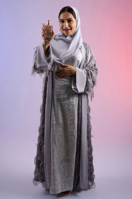 عطور عربية خليجية، الترويج للعطور والزيوت الطبيعية المحلية، مفهوم التعطر والتطيب، استخدام العود العطري، سيدة اماراتية تسوق للمنتجات العطرية، بورتريه لامرأه عربيه سعودية محجبة ترتدي العباءة تقوم برش العطر، الجسم بالطول الكامل، خلفية ملونة