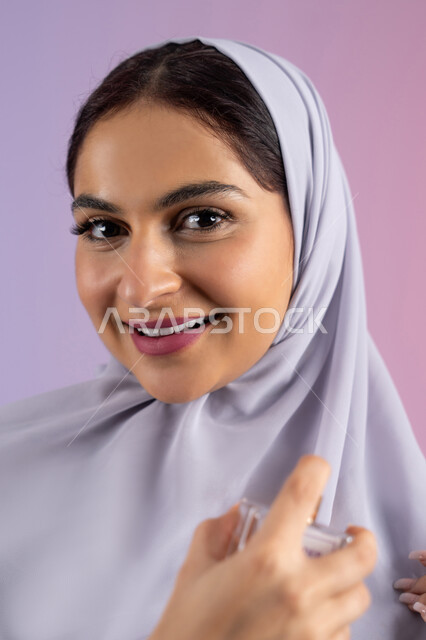 Marketing of international perfumes and natural oils, the concept of perfuming and fragrance, the use of fragrant oud, Arab Gulf perfumes, an Emirati woman shopping for aromatic products, a close-up portrait of a veiled Saudi Arab woman wearing an abaya spraying perfume, a colored background