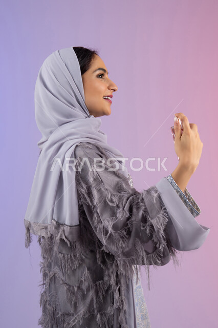 Arabian Gulf perfumes, use of fragrant oud, concept of perfuming and fragrance, marketing of international perfumes and natural oils, Emirati woman shopping for aromatic products, side portrait of a veiled Saudi Arabian woman wearing an abaya spraying perfume, colored background