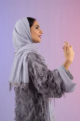 عطورات عربية خليجية، استخدام العود العطري، مفهوم التعطر والتطيب، التسويق للعطور والزيوت الطبيعية العالمية، سيدة اماراتية تسوق للمنتجات العطرية، بورتريه من الجانب لامرأه عربيه سعودية محجبة ترتدي العباءة تقوم برش العطر، خلفية ملونة