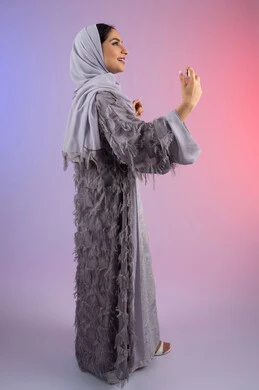 الترويج للعطور والزيوت الطبيعية المحلية، مفهوم التعطر والتطيب، عطورات عربية خليجية، استخدام العود العطري، سيدة اماراتية تسوق للمنتجات العطرية، بورتريه من الجانب لامرأه عربيه سعودية محجبة ترتدي العباءة تقوم برش العطر، الجسم بالطول الكامل، خلفية ملونة