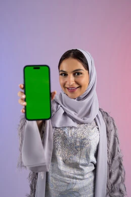 عرض تطبيقات الجوال عبر شاشة خضراء فارغة كروما، بورتريه مقرب لامرأة عربية خليجية اماراتية محجبة ترتدي العباءة تمسك بيدها الهاتف المحمول، شابة سعودية تستخدم جهاز تقني حديث ومتطور، النظر إلى الكاميرا بتعابير السرور والاعجاب، خلفية ملونة