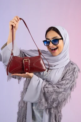 ايماءات السعادة والمتعة بامتلاك حقيبة جديدة، التسويق للمنتجات الاماراتية والماركات العالمية، عرض الأزياء والحقائب والاكسسوارات بالتصاميم الحديثة، بورتريه لامراة عربية خليجية اماراتية ترتدي نظارات شمسية عصرية، شابة سعودية تحمل بيدها حقيبة جلد فاخرة, خلفية ملونة