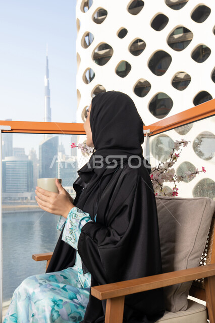 الاستمتاع بالمشروبات الساخنة، ايماءات المتعة والاسترخاء، قضاء وقت الفراغ باحتساء المشروب المفضل, تناول الأعشاب الشتوية الدافئة، امراة عربية خليجية اماراتية ترتدي العباءة والحجاب تقوم بشرب القهوة