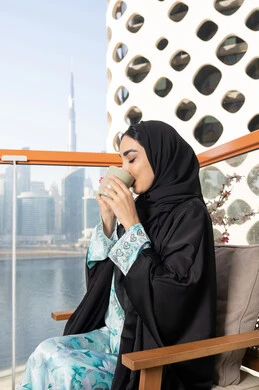 Eating warm winter herbs, an Emirati Gulf Arab woman wearing an abaya and hijab drinking coffee, enjoying hot drinks, expressions of pleasure and relaxation, spending free time sipping a favorite drink