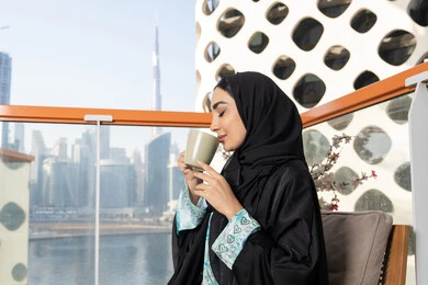Expressions of pleasure and relaxation, spending free time sipping a favorite drink, eating warm winter herbs, an Emirati Gulf Arab woman wearing an abaya and hijab drinking coffee, enjoying hot drinks