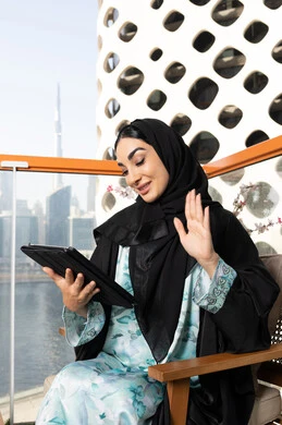 Making a video call, managing business and completing required tasks via tablet, a female profession and job, an Emirati Gulf Arab woman wearing an abaya and hijab using a portable tablet, using a modern and advanced technical device, working remotely abroad
