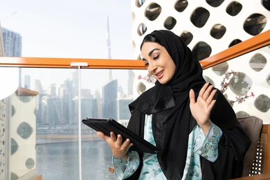 Making a video call, managing business and completing required tasks via tablet, a female profession and job, an Emirati Gulf Arab woman wearing an abaya and hijab using a portable tablet, using a modern and advanced technical device, working remotely abroad