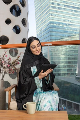 Business management and completing required tasks via tablet, a female profession and job, an Arab Gulf Emirati woman wearing an abaya and hijab using a portable tablet, using a modern and advanced technical device, working remotely abroad