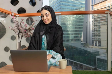 ايماءات التركيز والاندماج، ادارة الأعمال وانجاز المهام المطلوبة، العمل عن بعد،  مهنة ووظيفة نسائية، إمرأة عربية خليجية اماراتية محجبة ترتدي العباءة والحجاب تستخدم الحاسوب المحمول، استخدام جهاز تقني حديث ومتطور