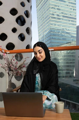Gestures of focus and integration, business management and completing required tasks, remote work, female profession and job, veiled Arab Gulf Emirati woman wearing abaya and hijab using laptop, using a modern and advanced technical device