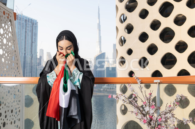 Union Day, December 2, Emirati Gulf Arab woman wearing hijab and abaya holding the UAE flag, Flag Day, November 3, love and pride of the homeland, gestures of happiness, pride and honor, remembering the UAE National Day 1971