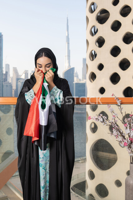 يوم العلم 3 نوفمبر، حب الوطن والاعتزاز به، ايماءات السعادة والفخر والاعتزاز، استذكار اليوم الوطني الاماراتي 1971، ذكرى تأسيس الاتحاد 2 ديسمبر، إمراة عربية خليجية إماراتية ترتدي الحجاب والعباءة تمسك بيدها علم الإمارات العربية المتحدة