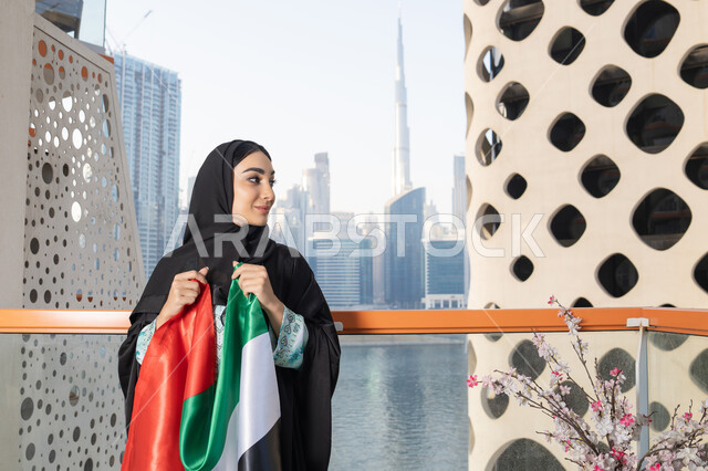 استذكار اليوم الوطني الاماراتي 1971، ذكرى تأسيس الاتحاد 2 ديسمبر، إمراة عربية خليجية إماراتية ترتدي الحجاب والعباءة تمسك بيدها علم الإمارات العربية المتحدة ، يوم العلم 3 نوفمبر، حب الوطن والاعتزاز به، ايماءات السعادة والفخر والاعتزاز