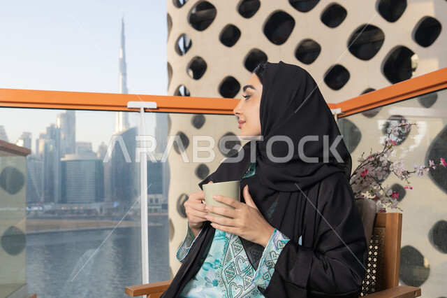 تناول الأعشاب الشتوية الدافئة، مطاعم  وكافيهات في الامارات العربية المتحدة، قضاء وقت الفراغ باحتساء المشروب المفضل، الاستمتاع بالمشروبات الساخنة، صورة مقربة لامراة اماراتية ترتدي العباءة والحجاب تجلس على اريكة مريحة تقوم بشرب القهوة في المقهى
