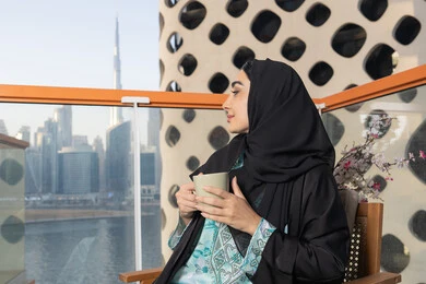 Restaurants and cafes in the United Arab Emirates, spending free time sipping your favorite drink, eating warm winter herbs, enjoying hot drinks, a close-up photo of an Emirati woman wearing an abaya and hijab sitting on a comfortable sofa drinking coffee in a cafe