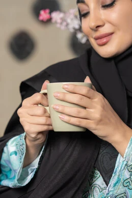 Cafes and restaurants in the United Arab Emirates, spending free time sipping your favorite drink, eating warm winter herbs, enjoying hot drinks, a close-up of an Emirati woman wearing an abaya and hijab sitting on a comfortable sofa drinking coffee in a cafe