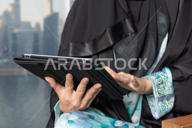 ادارة الأعمال وانجاز المهام المطلوبة، العمل عن بعد،  مهنة ووظيفة نسائية، إمرأة عربية خليجية اماراتية محجبة ترتدي عباءة تستخدم الحاسوب المحمول، استخدام جهاز تقني حديث ومتطور، ايماءات التركيز والاندماج