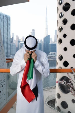 هوية اليوم الوطني الإماراتي 51، الإحتفال باليوم الوطني الإماراتي، يوم استقلال الإمارات، الاعتزاز والفخر بإنجازات البلاد، الحب والانتماء للوطن، رجل عربي خليجي إماراتي يرتدي الكندورة والغترة البيضاء يقوم بتقبيل علم الإمارات العربية المتحدة