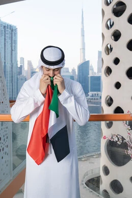 Celebrating UAE National Day, UAE National Day 51 identity, UAE Independence Day, pride in the country's achievements, love and belonging to the homeland, an Emirati Gulf Arab man wearing a white kandura and ghutra kissing the UAE flag