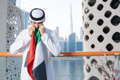 Celebrating UAE National Day, UAE National Day 51 identity, UAE Independence Day, pride in the country's achievements, love and belonging to the homeland, an Emirati Gulf Arab man wearing a white kandura and ghutra kissing the UAE flag