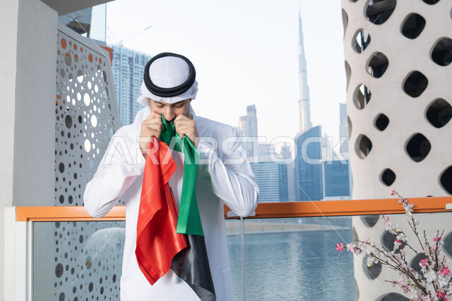 هوية اليوم الوطني الإماراتي 51، الإحتفال باليوم الوطني الإماراتي، يوم استقلال الإمارات، الاعتزاز والفخر بإنجازات البلاد، الحب والانتماء للوطن، رجل عربي خليجي إماراتي يرتدي الكندورة والغترة البيضاء يقوم بتقبيل علم الإمارات العربية المتحدة